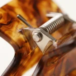 Close-up of the steel spring bar and hinge pin fitted into the body of a tortoiseshell acetate hair claw clip
