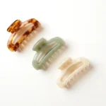 Cellulose acetate hair claw clips in amber tortoiseshell, sage green and ivory on a neutral background
