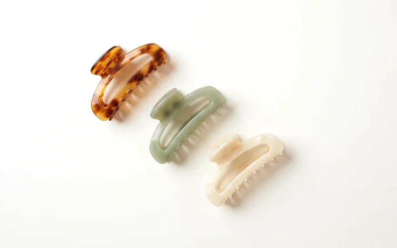 Cellulose acetate hair claw clips in amber tortoiseshell, sage green and ivory on a neutral background