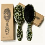 Two acetate cushion hair brushes beside plain kraft boxes marked for customisable logo printing