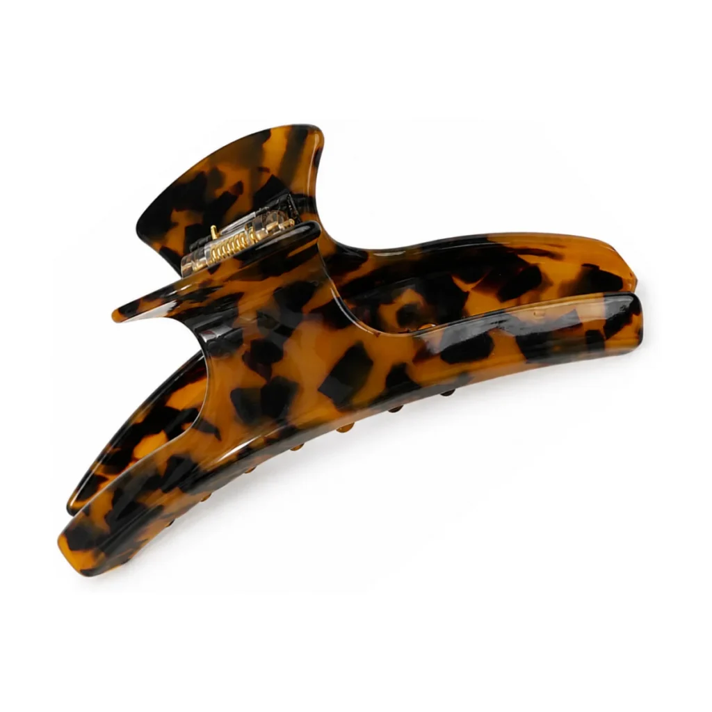 Dark tortoiseshell acetate claw clip on a white background, showing the hooked upper arm and the deep amber and near-black layers running through the sheet