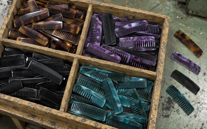 A divided wooden workshop tray filled with short handle-free acetate pocket combs in tortoiseshell, purple marble, black and teal