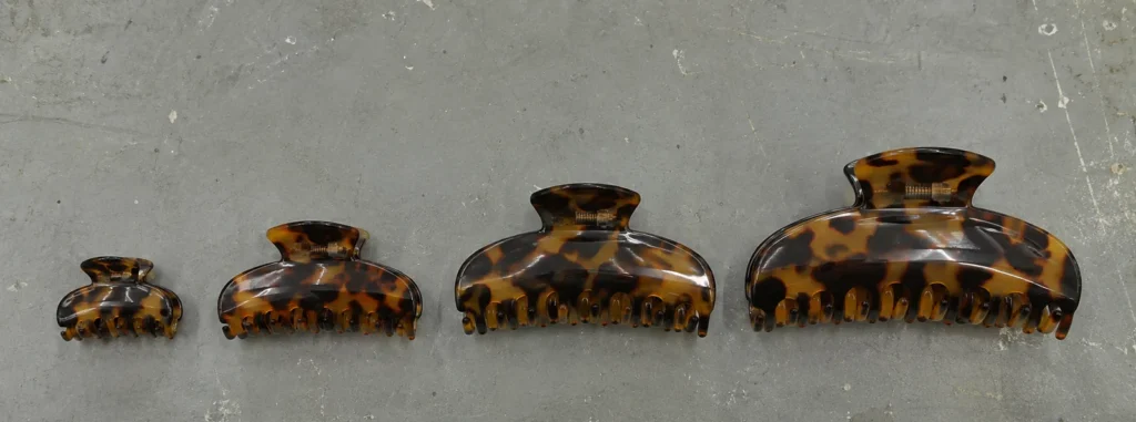 Four acetate claw clips in the same tortoiseshell pattern laid in a row from smallest to largest, showing the size range of one shape family
