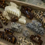 Wooden workshop tray filled with acetate claw clips in tortoiseshell, pearl and marble patterns across mixed sizes