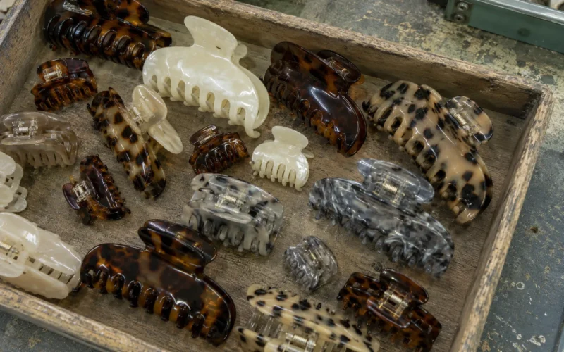 Wooden workshop tray filled with acetate claw clips in tortoiseshell, pearl and marble patterns across mixed sizes