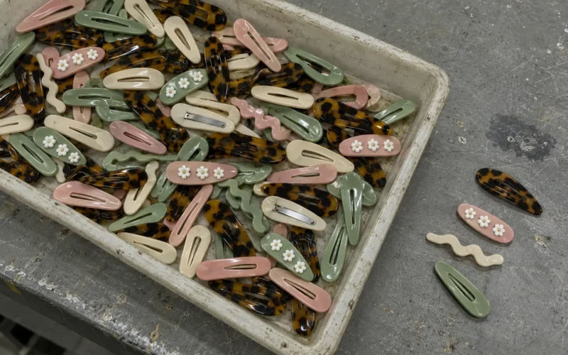 Tray of acetate snap hair clips in tortoiseshell, cream, pink and sage green, two turned over to show the steel snap strip
