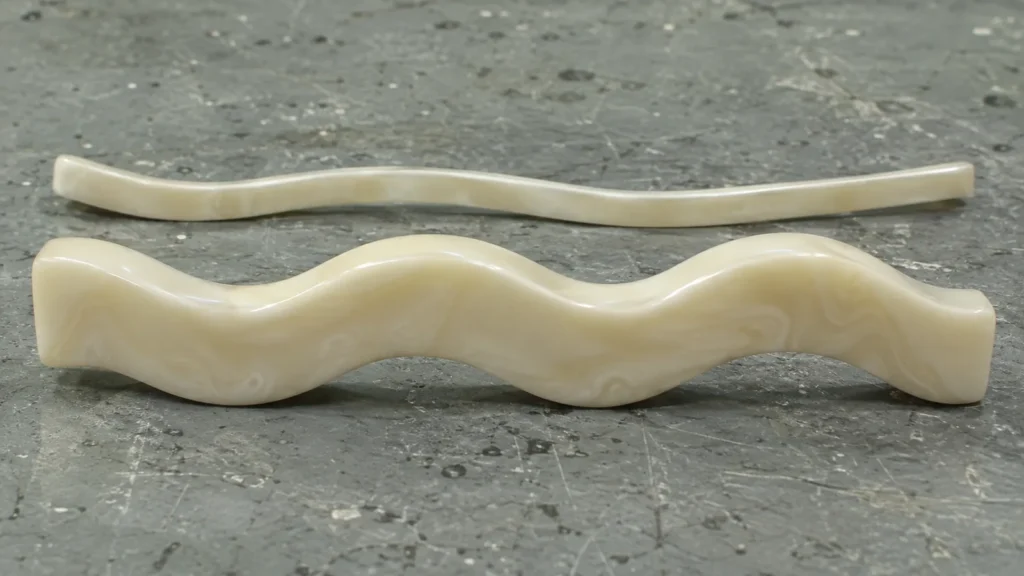 Side view of two cream wavy hair clips: a thick clip whose side edge follows the wave, and a thin bent strip that is flat from the side